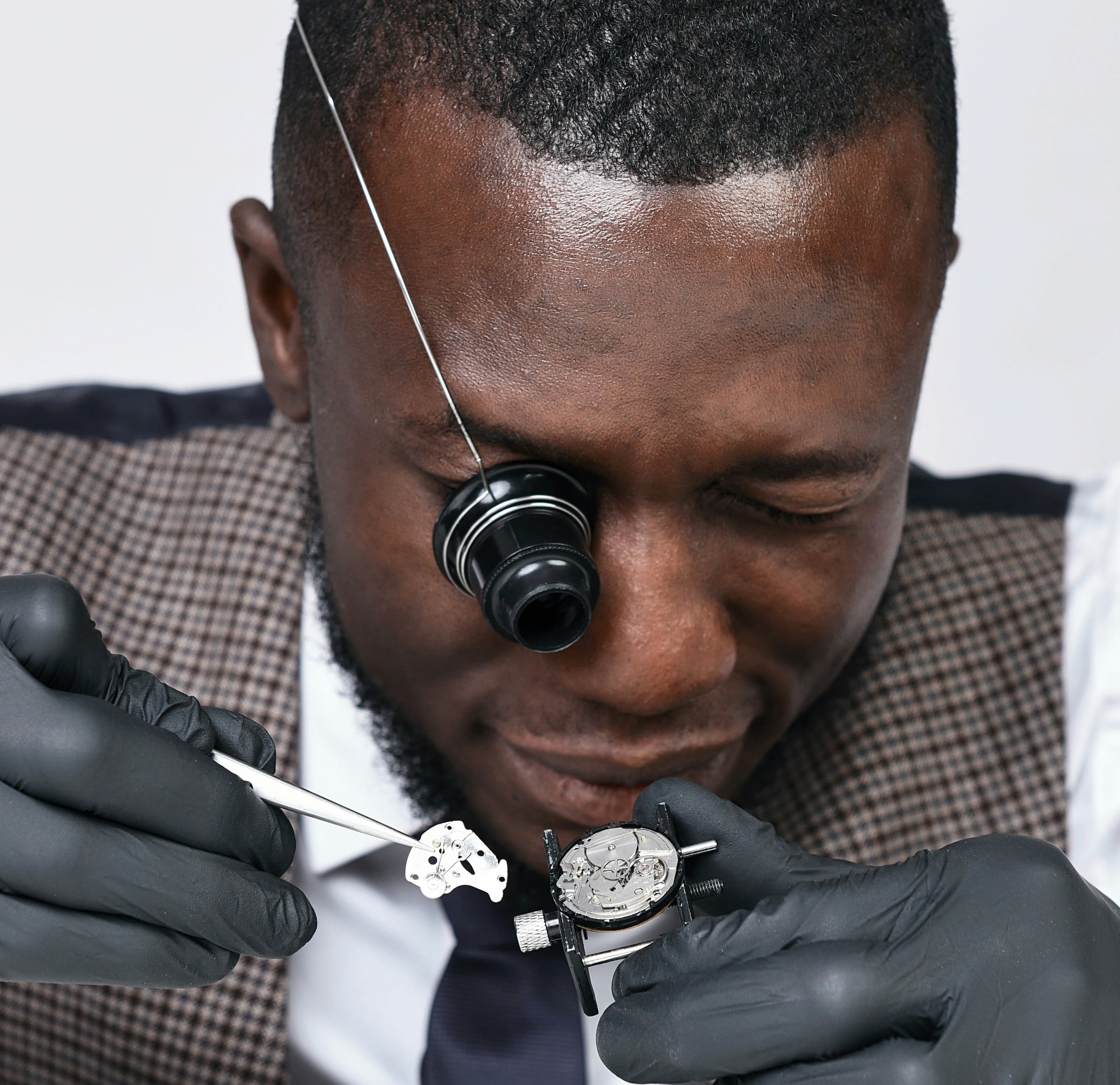 A watchmaker with a loupe inspecting a movement held in a vice